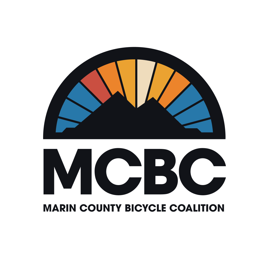 Marin County Bicycle Coalition Logo with the letters MCBC under the silhouetted peaks of two mountains inside a spoke with a blue to orange sky.