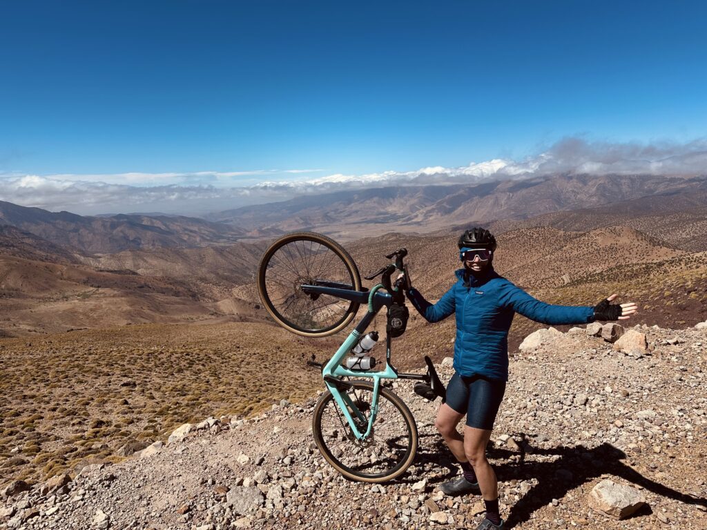 Person standing an arm out and supporting a bike in a desert overlook.