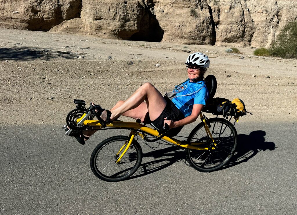 Donna seated on her recombinant bike while riding on a road in the desert.