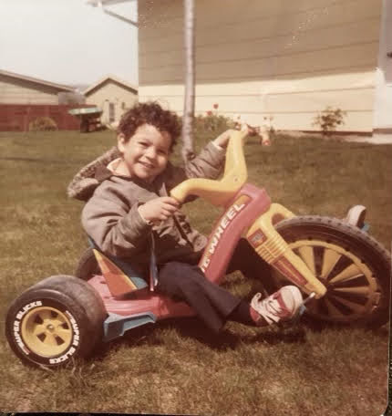 A weathered photo of Frankie on a trike in a yard.