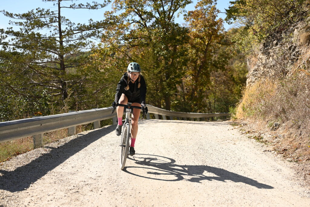 Naomi Schroeder cycling on a mountain pass with a guard rail beside her.