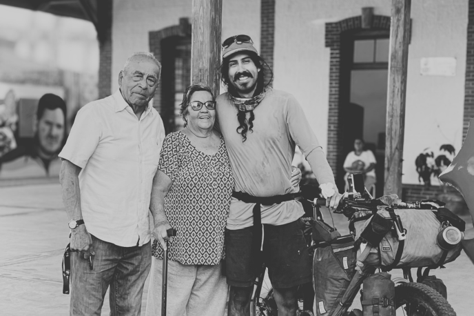 Luis standing with their parents and bike packing bike loaded up and smiling for the camera.