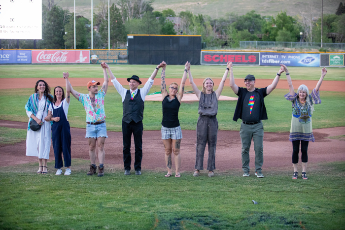 A group of people are holding hands aloft during a curtain call after a storytelling event. They are dressed in casual clothing appropriate for an activity. photo credit kmr studios.